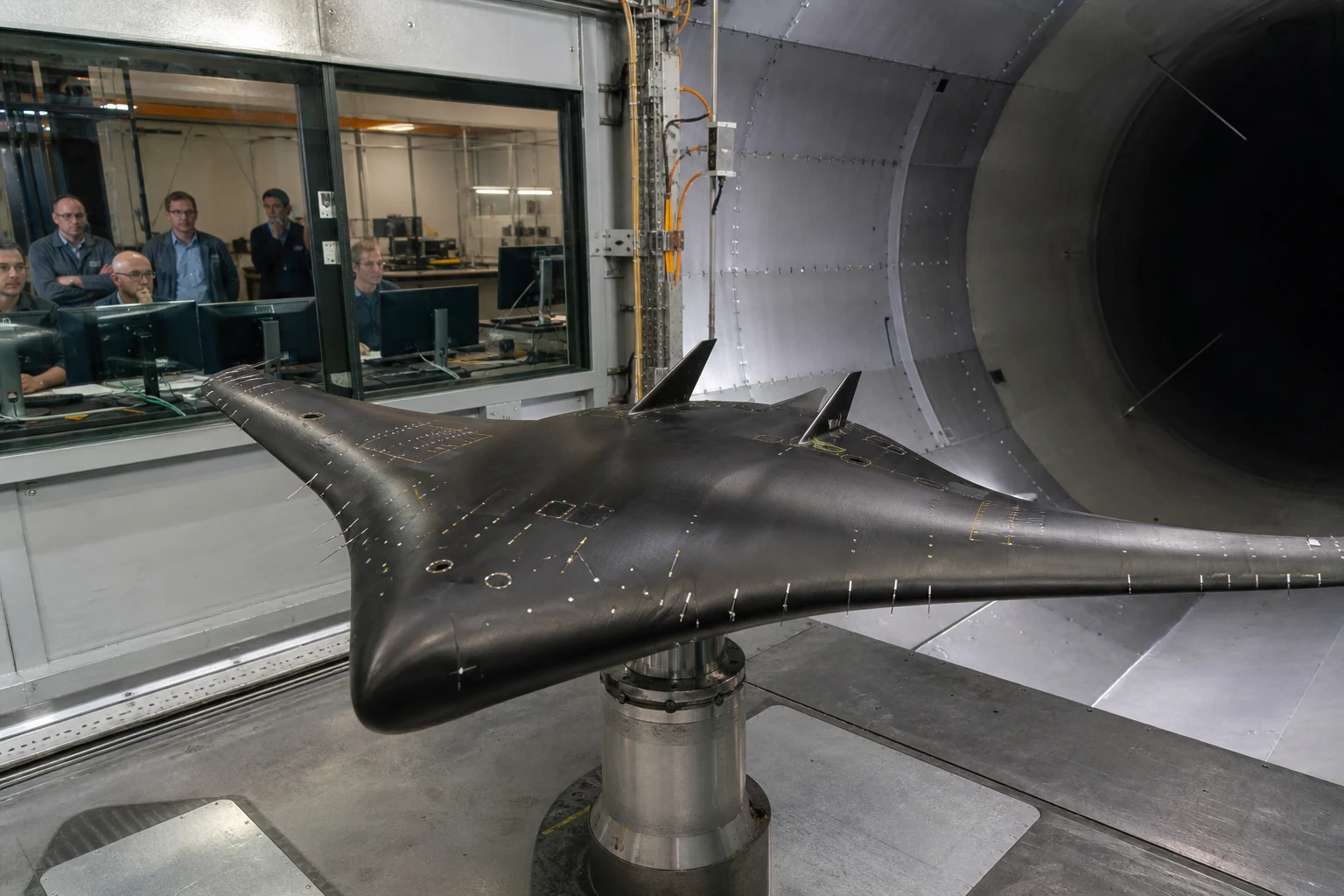 Instrumented blended wing body scale model mounted in a wind tunnel while aerospace engineers monitor the test